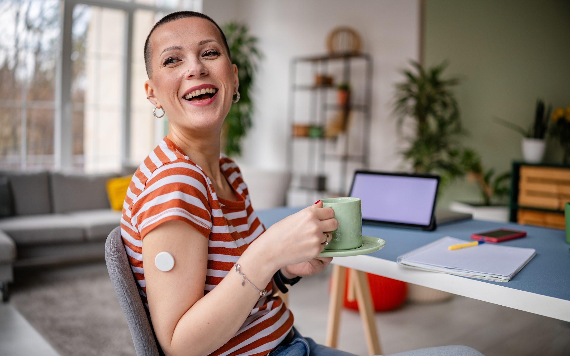 Smiling woman with short hair holding green coffee cup at desk with laptop in bright modern office space