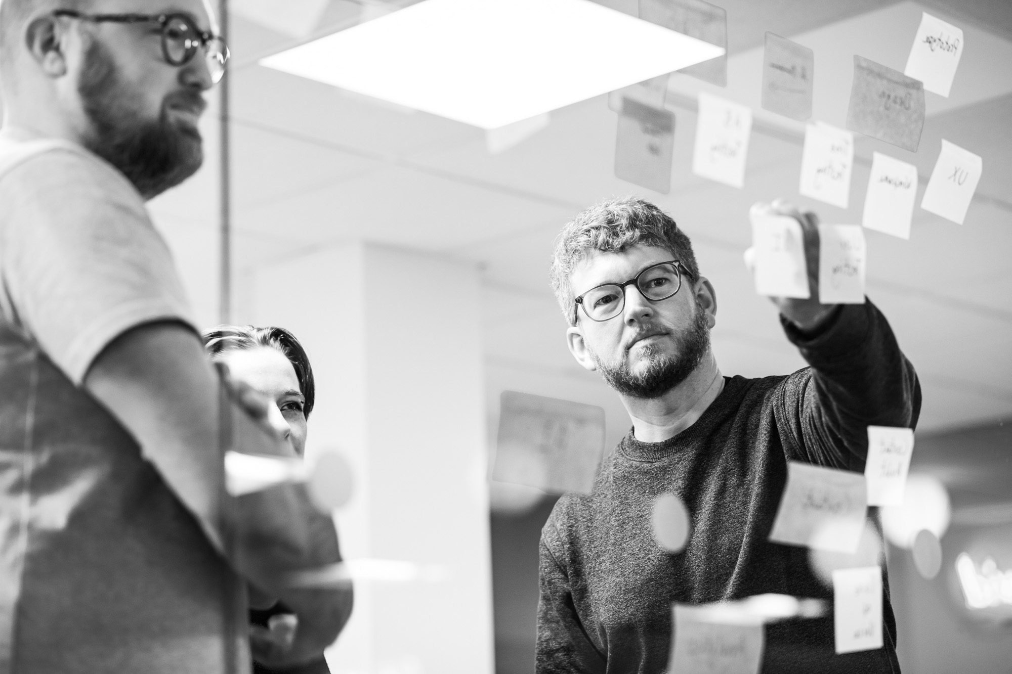 Team members collaborating at whiteboard with sticky notes in black and white office setting