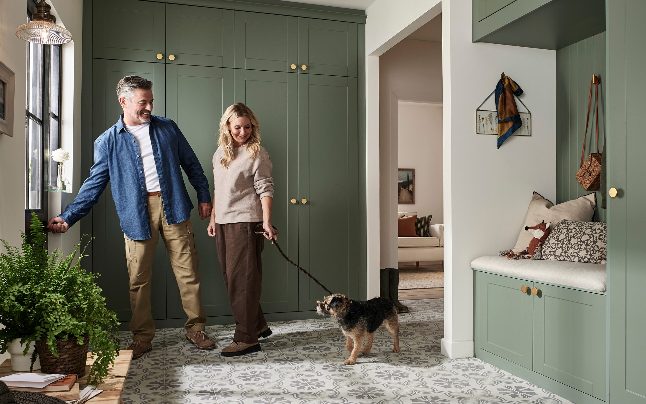 Couple walking small dog through modern green mudroom with built-in storage and bench seating