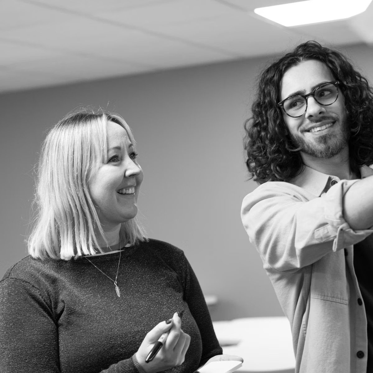 Two colleagues collaborating in an office setting, woman with blonde bob haircut and man with curly hair and glasses