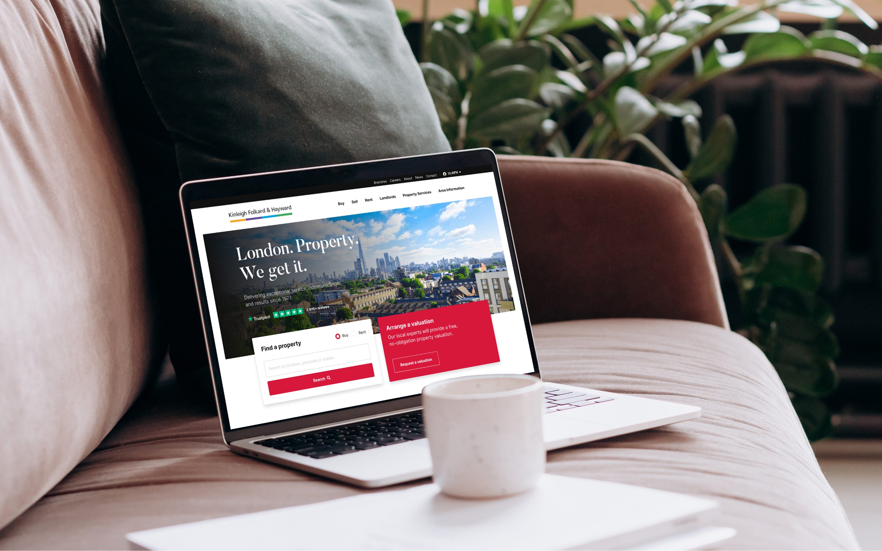 Laptop displaying Kinleigh Folkard & Hayward property website with London skyline background on comfortable chair