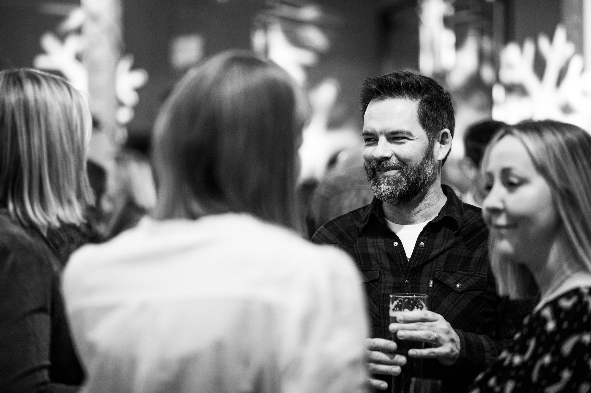 Man with beard smiling and holding drink at social gathering in black and white