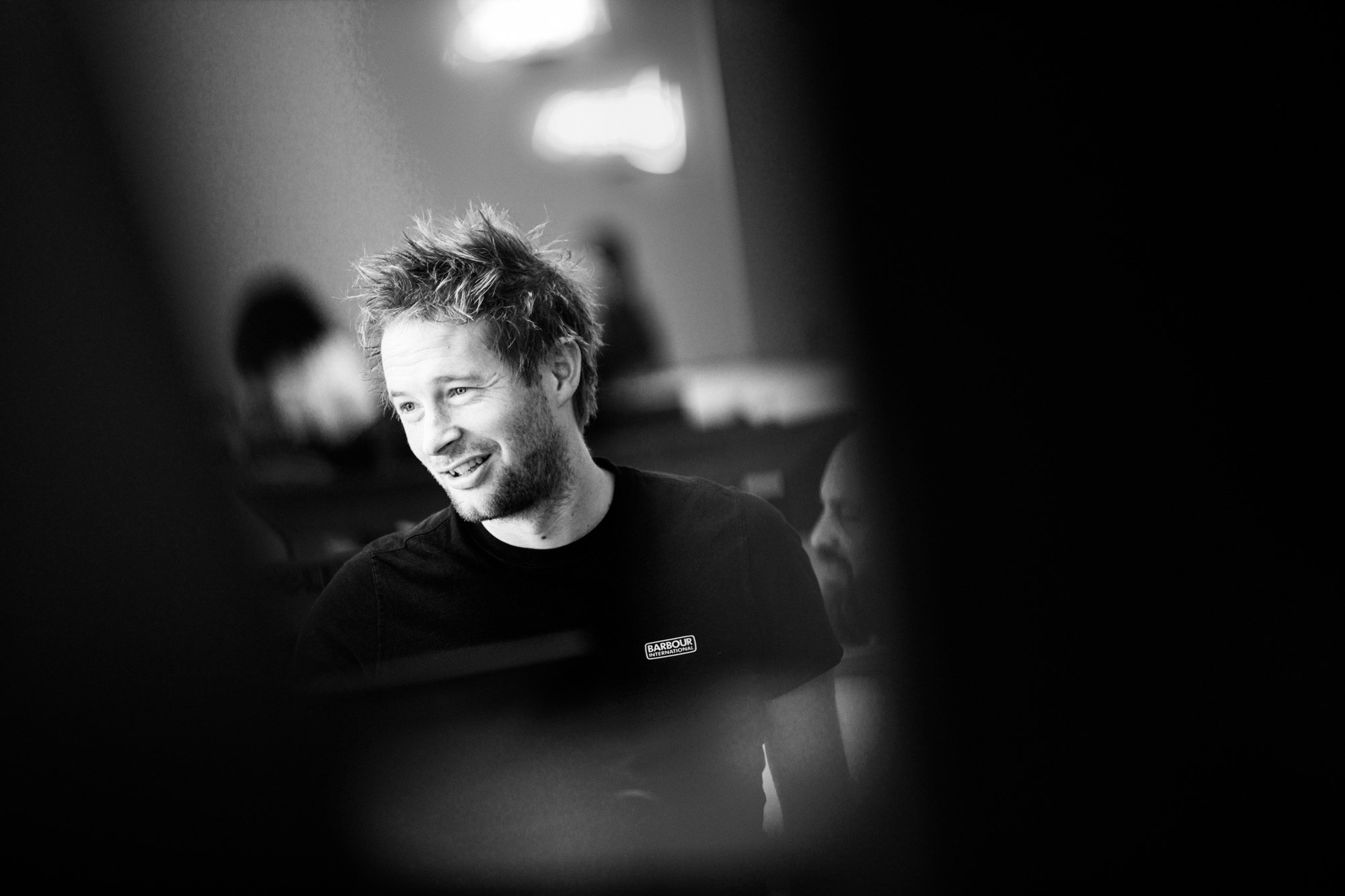 Young man with tousled hair smiling in black and white photo with blurred background